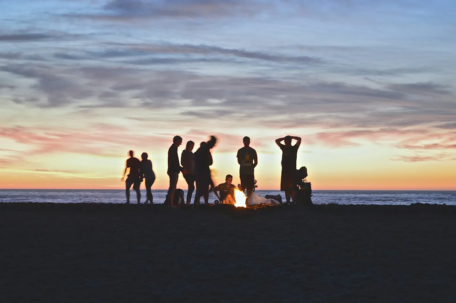 Friends gathered around a campfire on the beach at dusk